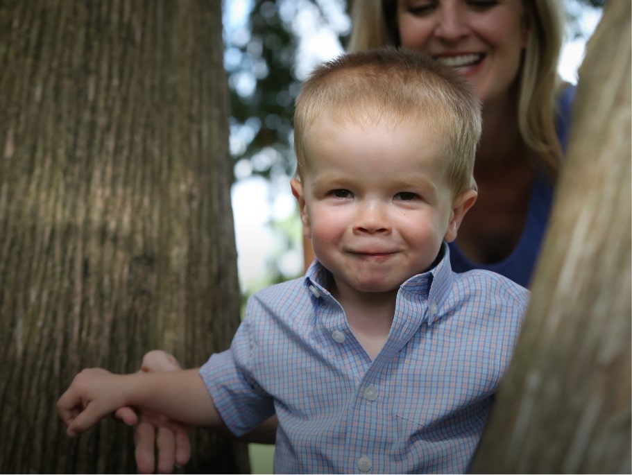 Portrait of young child in trees and mother in the background