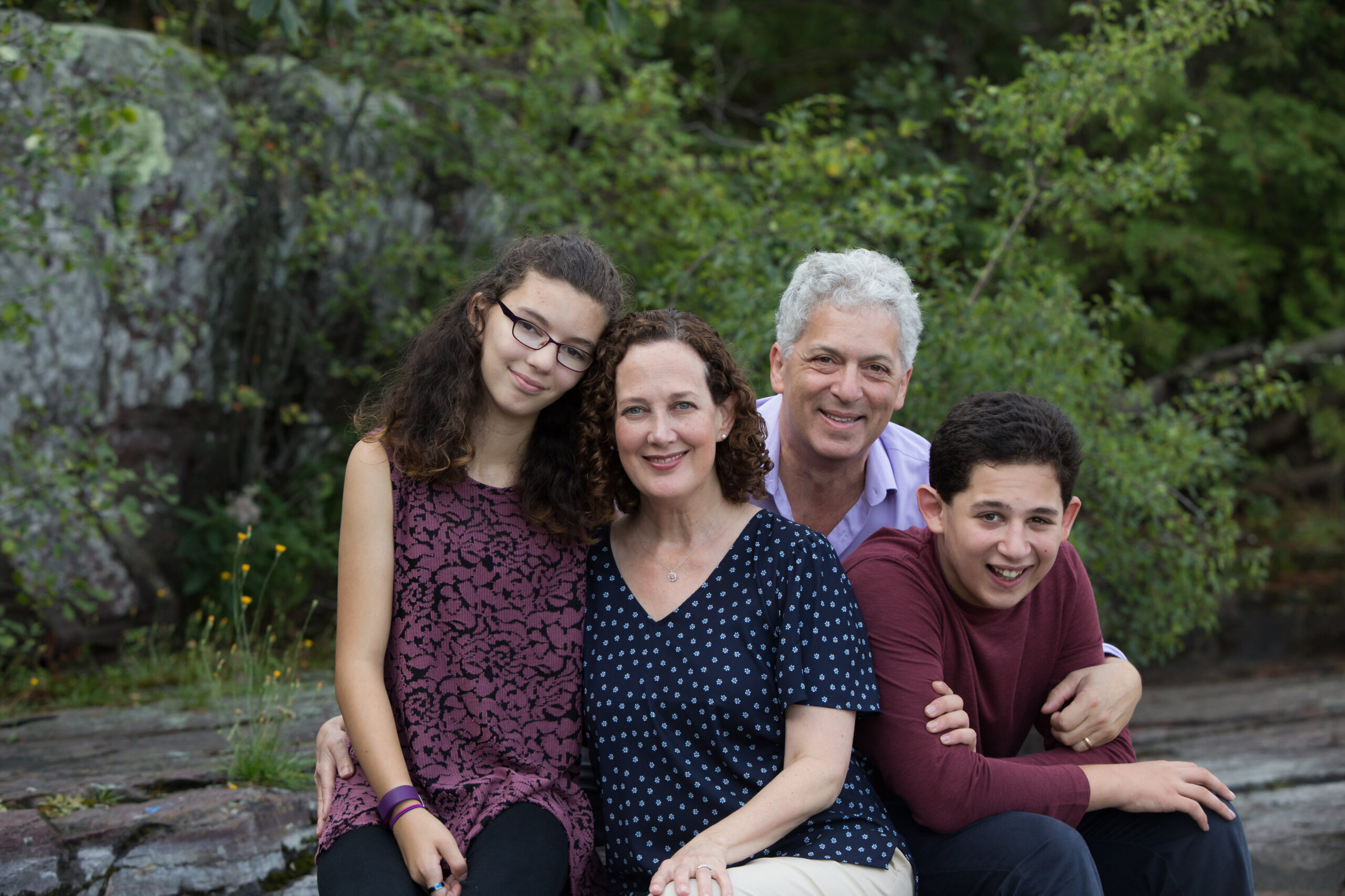 Family portrait sitting on rocks with trees in the background